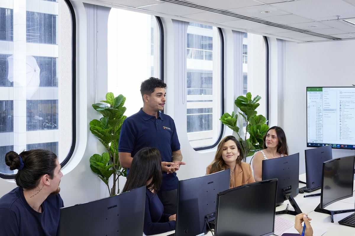A trainer leading a small group of students at computer workstations in a modern classroom
