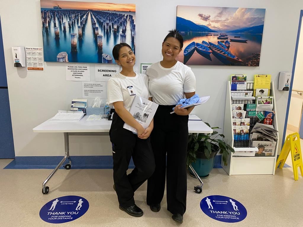 Two trainee carers smiling at the entrance of an aged care facility during placement
